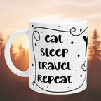 Weiße Keramiktasse mit Schriftzug „Eat Sleep Travel Repeat“, beidseitigem Druck und illustrativem Flugzeug-Motiv in der Mitte.