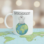 Weiße Keramiktasse mit Geist auf Weltkugel und Schriftzug „Entdeckergeist“. Lustige Tasse für Reisefans und Kinder.