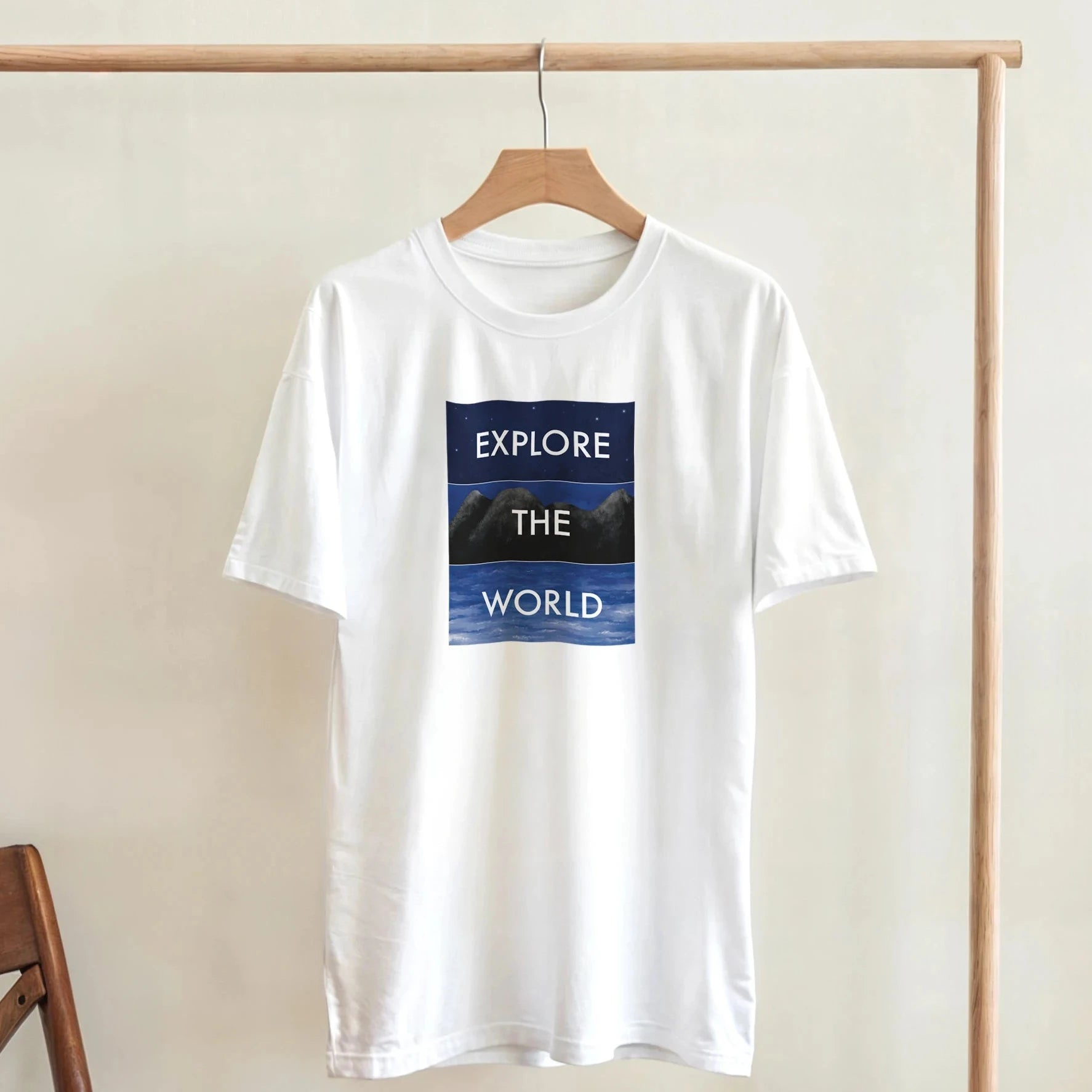 T-Shirt mit illustriertem Motiv aus Himmel, Bergen und Meer und dem Schriftzug „Explore the World“. Künstlerischer Stil für Entdecker.