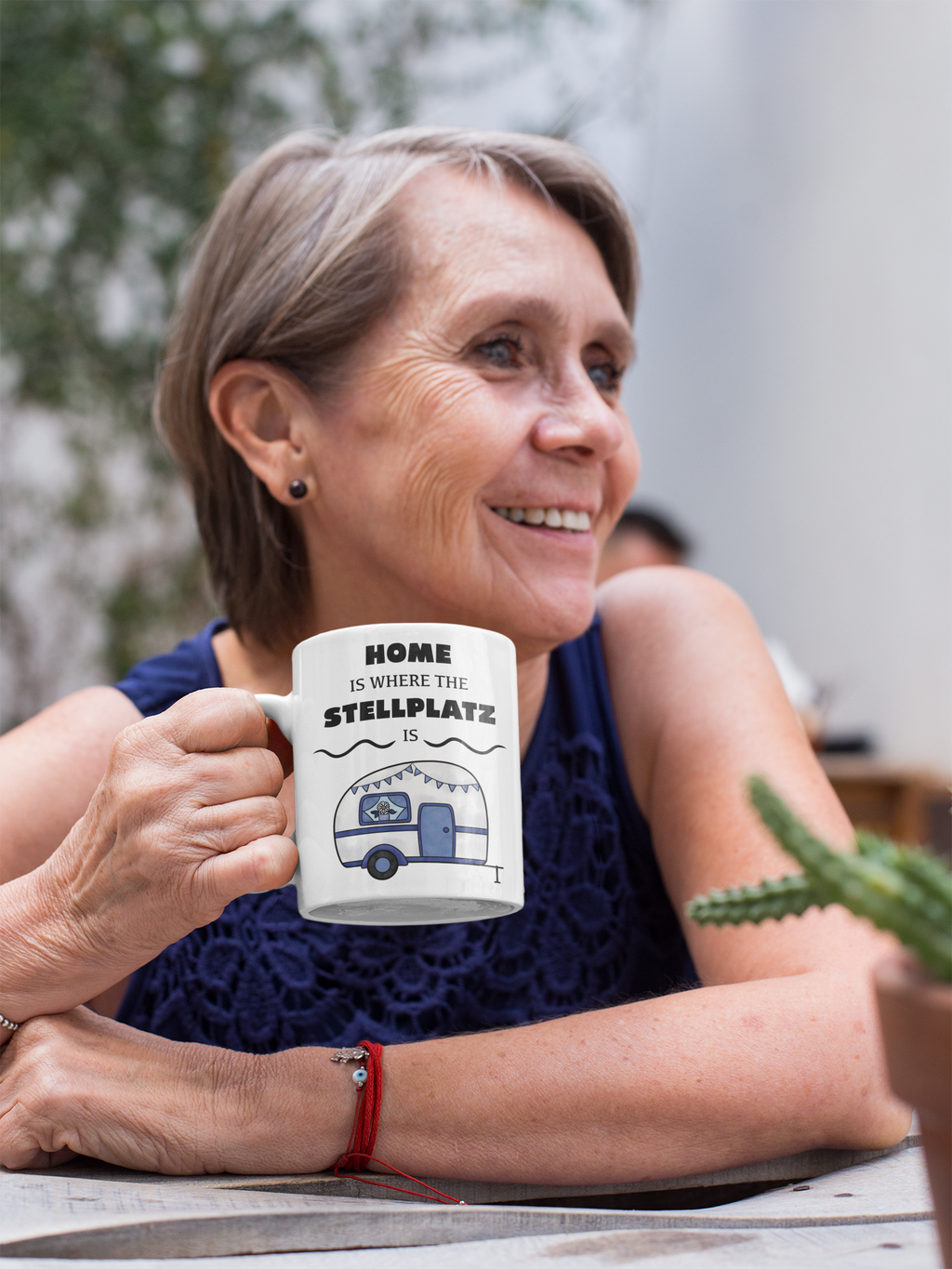 Weiße Tasse mit blau-weißem Wohnwagen und Spruch „Home is where the Stellplatz is“. Camping-Tasse für Wohnmobil- und Vanlife-Fans.