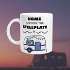 Weiße Tasse mit blau-weißem Wohnwagen und Spruch „Home is where the Stellplatz is“. Camping-Tasse für Wohnmobil- und Vanlife-Fans.