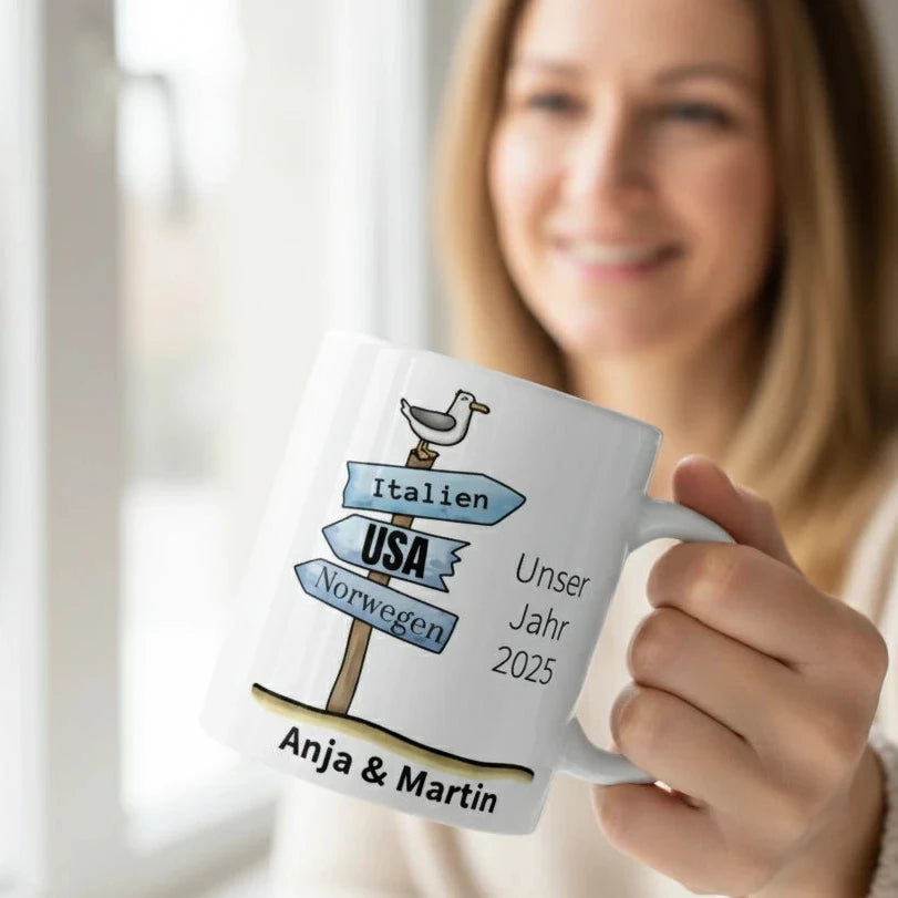 Weiße Keramiktasse mit bunten Wegweisern, Möwe, personalisiertem Namen und Jahr. Reise-Motiv mit Zielen wie Italien, USA und Norwegen.